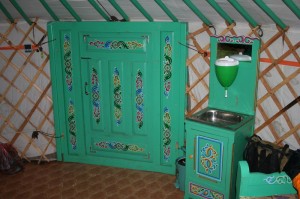 The entrance to the yurt from the inside. To the right of the door is the wash basin. The receptacle above the basin can be filled with water. The waste water flows into a bucket underneath the basin.